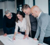 A group of four professionals collaborate around a table, analyzing charts in a modern office, highlighting teamwork and focus.
