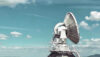 Large satellite communication antenna and communications tower under a blue sky.