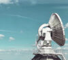 Large satellite communication antenna and communications tower under a blue sky.