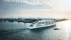 Cruise ship sailing through Hamburg Harbor with container terminals and cranes in the background.