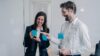 Two business professionals collaborating with sticky notes on a glass wall in a modern office.