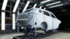 White passenger vehicle body shell undergoing inspection in an illuminated automotive production facility.