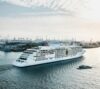 Cruise ship sailing through Hamburg Harbor with container terminals and cranes in the background.
