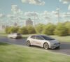 Electric passenger vehicle powered by a solid-state battery driving past wind turbines.