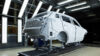 White passenger vehicle body shell undergoing inspection in an illuminated automotive production facility.