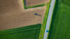 Aerial view of a tractor working on farmland beside a road and green fields.