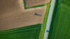 Aerial view of a tractor working on farmland beside a road and green fields.