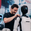 A man interacting with a humanoid service robot at a technology exhibition, with another robot visible in the background.